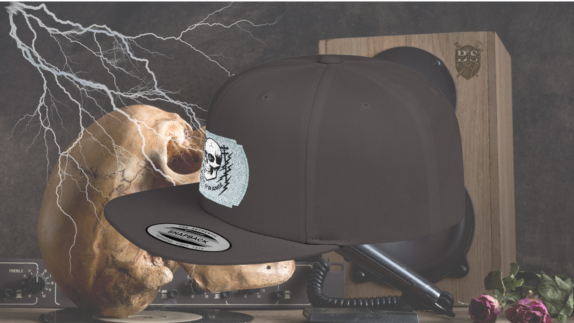 Shock, grit, and street-ready energy.
The Built Strange Skull & Power Lines Snapback Hat features a bold embroidered-style patch: a grinning skull with electric-blue eyes, flanked by utility poles and jagged lightning bolts. This design embodies the raw power and fearless pride of the trade, making it more than just a hat—it’s a statement.
Built on a structured snapback silhouette, it’s equal parts workwear toughness and streetwear edge.