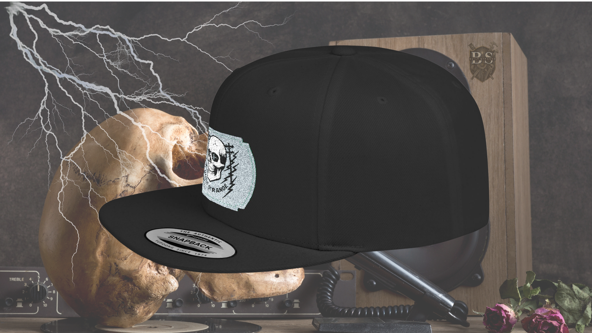 Shock, grit, and street-ready energy.
The Built Strange Skull & Power Lines Snapback Hat features a bold embroidered-style patch: a grinning skull with electric-blue eyes, flanked by utility poles and jagged lightning bolts. This design embodies the raw power and fearless pride of the trade, making it more than just a hat—it’s a statement.
Built on a structured snapback silhouette, it’s equal parts workwear toughness and streetwear edge.