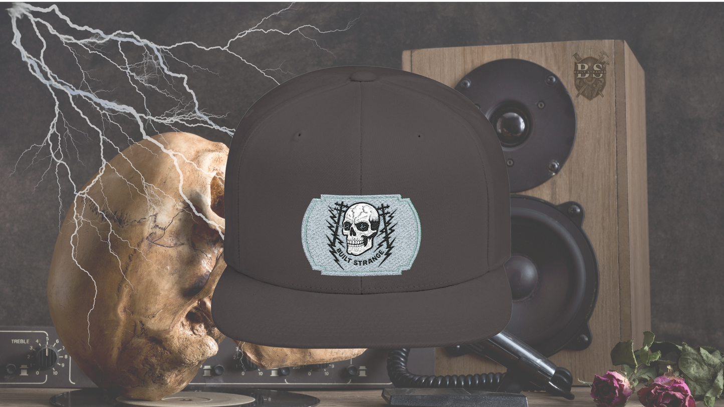 Shock, grit, and street-ready energy.

The Built Strange Skull &amp; Power Lines Snapback Hat features a bold embroidered-style patch: a grinning skull with electric-blue eyes, flanked by utility poles and jagged lightning bolts. This design embodies the raw power and fearless pride of the trade, making it more than just a hat—it’s a statement.

Built on a structured snapback silhouette, it’s equal parts workwear toughness and streetwear edge.
