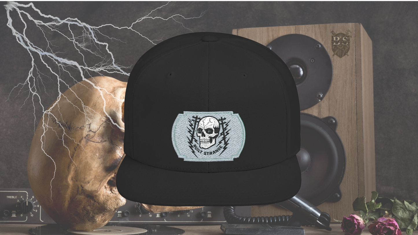 Shock, grit, and street-ready energy.

The Built Strange Skull &amp; Power Lines Snapback Hat features a bold embroidered-style patch: a grinning skull with electric-blue eyes, flanked by utility poles and jagged lightning bolts. This design embodies the raw power and fearless pride of the trade, making it more than just a hat—it’s a statement.

Built on a structured snapback silhouette, it’s equal parts workwear toughness and streetwear edge.
