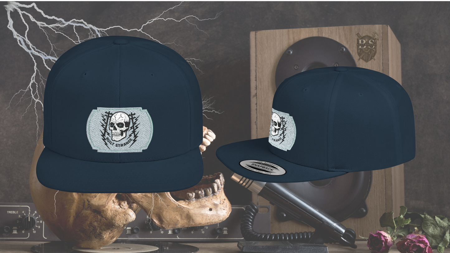 Shock, grit, and street-ready energy.

The Built Strange Skull &amp; Power Lines Snapback Hat features a bold embroidered-style patch: a grinning skull with electric-blue eyes, flanked by utility poles and jagged lightning bolts. This design embodies the raw power and fearless pride of the trade, making it more than just a hat—it’s a statement.

Built on a structured snapback silhouette, it’s equal parts workwear toughness and streetwear edge.